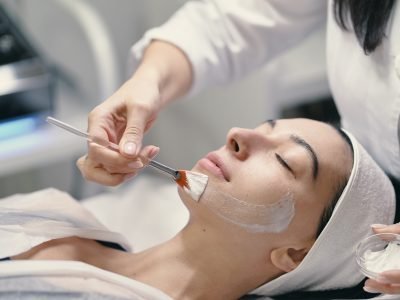 People, beauty, spa, cosmetology and skin care concept - Cosmetologist applying cream on a woman beautiful face with a cosmetologist brush.